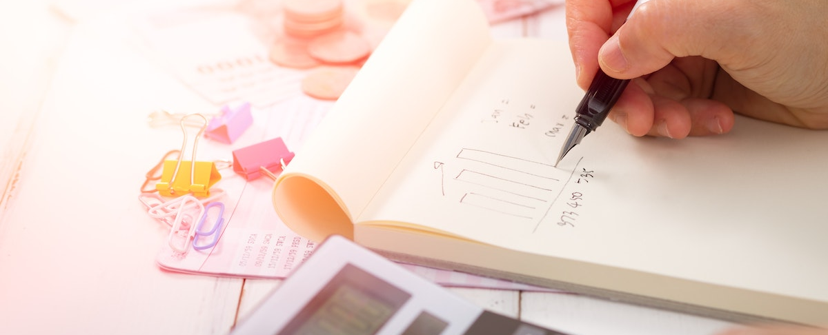 person writing in notebook and using calculator